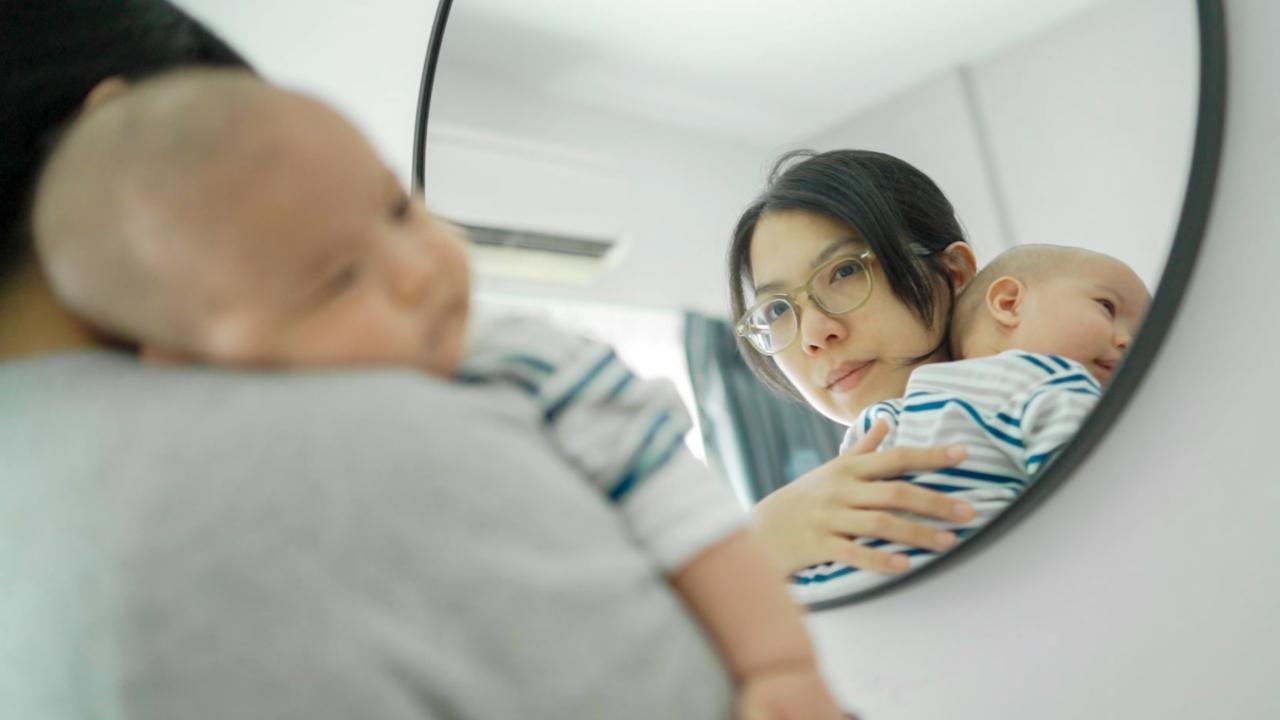 A woman holding a baby and looking into a mirror